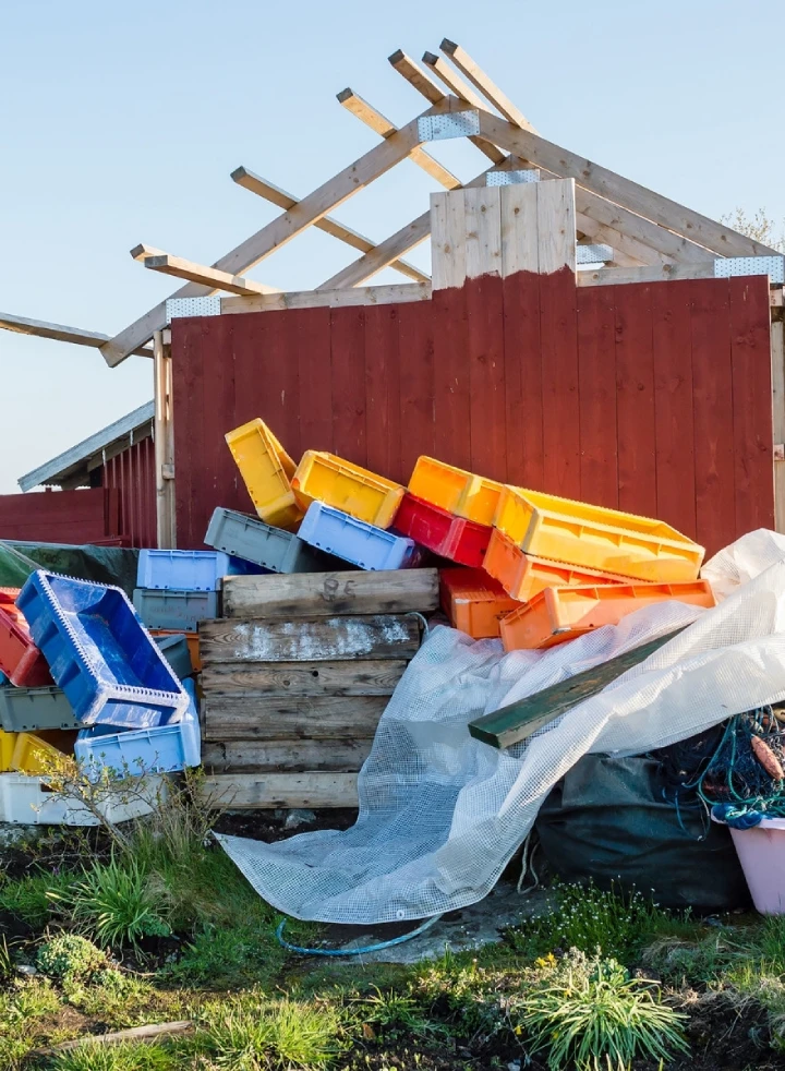 Colorful stacked crates next to a partially constructed wooden disaster relief shed under a clear sky.